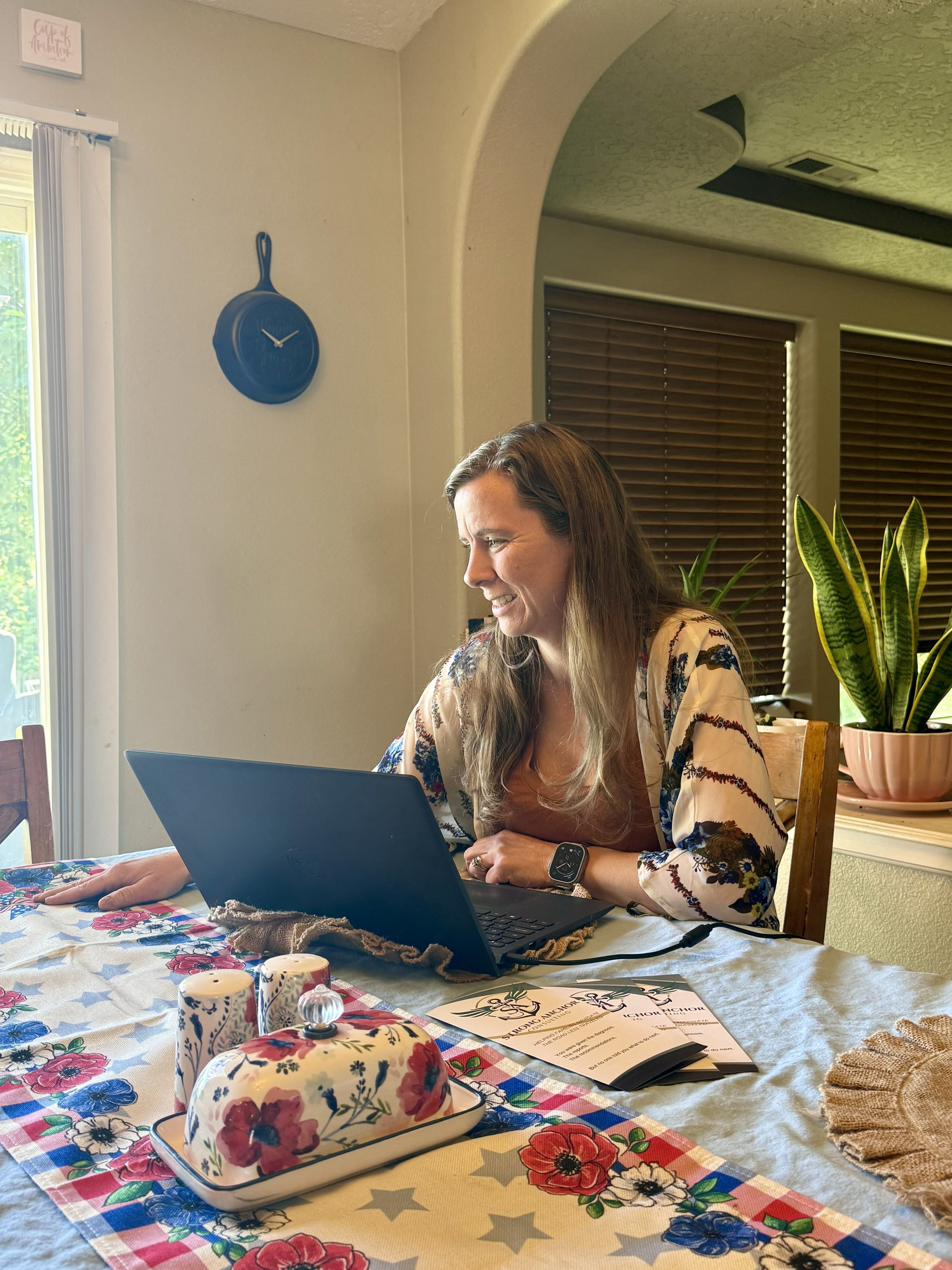 Smiling woman in floral kimono works on a laptop at a table with business brochures.